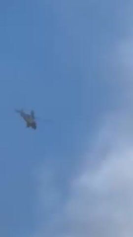 The video shows a helicopter flying against a cloudy sky. The helicopter is initially small in the frame but gradually gets larger as it approaches. The clouds vary from light to darker gray, obscuring the details of the helicopter.