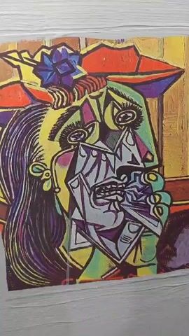 The video is a close-up, static shot of a framed picture of a painting. The painting is a cubist-style depiction of a crying woman. The woman has exaggerated features, including large, tearful eyes, a distorted mouth, and fragmented facial planes. She is wearing a colorful hat adorned with a blue flower. The background of the painting appears to be a striped pattern. The frame of the picture is visible, and it seems to be affixed to a wall. The lighting is somewhat dim, and the focus is sharp on the painting.