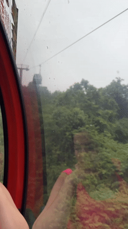 Woman rides red cable car through lush Yongding scenery