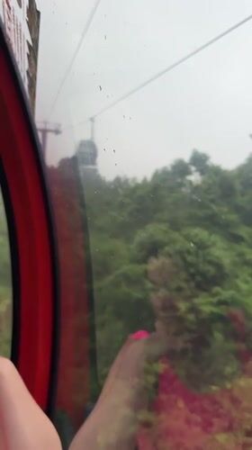Woman rides red cable car through lush Yongding scenery