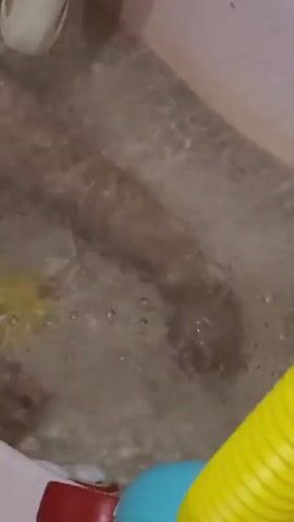 The media file shows a close-up view of a wet, tiled floor, likely in a bathroom or shower area. A white bottle of baby shampoo, with a picture of a baby on the label, is visible in the upper left corner. The bottle appears to be tipping over, spilling its contents onto the floor. Yellow liquid can be seen pooling on the floor, creating a frothy mixture with the water and shampoo. Bubbles are forming on the surface of the water. In the lower right of the frame, parts of colorful children's toys are visible, including a yellow corrugated tube and a blue ball. The overall impression is that of a playful, albeit messy, bath time scene, possibly for a young child. The lighting suggests it is daytime, but there are no clear indications of the time of day or weather conditions. The location is specified as Mykilske, Ukraine. There is text on the shampoo bottle, but it is too blurry to read clearly.