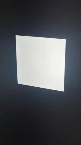 The media file is a short video clip showcasing a square light fixture mounted on a wall. The light is bright white and appears to be illuminated. Below the light, a white air conditioning unit is visible. The surrounding environment is dark, suggesting the video was filmed in a low-light setting, possibly at night or indoors with the main lights off. The camera angle is angled upwards, looking towards the ceiling and the light fixture. The scene appears to be a room, likely within a building. There is no visible text in the video. The overall mood is minimalist and focuses solely on the illuminated light panel and the air conditioner. The location is identified as Gülnar, Turkey, though there are no specific visual cues in the video to confirm this.