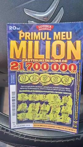 The media shows a close-up of a lottery ticket titled "PRIMUL MEU MILION" (My First Million) from "LOTERIA NATIONALA." The ticket is predominantly blue and yellow, with large, bold lettering emphasizing "MILION." Below this, it states "CASTIGURI IN SUMA DE 21,700,000 LEI" (Winnings totaling 21,700,000 LEI). The ticket features several circular areas that appear to be scratch-off zones, with numbers like "31," "21," "40," "39," and "32" visible in the top row of winning numbers. The lower section displays rows of scratched-off areas, revealing various numbers and prize amounts, including "50,000 LEI" and "200 LEI." Text below these areas reads "NUMERELE DUMNEAVOASTRA / ВАШИ ЧИСЛА" (Your numbers / Your numbers). The bottom of the ticket has a serial number "37-014346-004" and the text "RAZUIȚI AICI / СОТРИТЕ ЗДЕСЬ" (Scratch here / Scratch here). The ticket is lying on a dark, textured surface, possibly a car seat, with glimpses of a metallic car interior element at the top of the frame. The lighting suggests it might be daytime. The overall impression is one of excitement and anticipation associated with lottery games. The text is in Romanian and possibly Cyrillic script, indicating a Moldovan context.