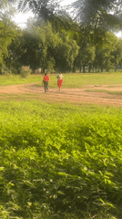 Two people walk dirt path through grassy field in Keffi