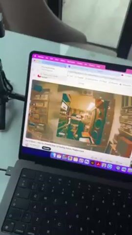 A person is holding a hand in front of a laptop displaying a YouTube video by Jazzy Orbison titled “Rare Too (FREDDIE GIBBS) ft. Lil Yachty, Future, Playboi Carti.” The video shows a room filled with vintage stereo equipment. The laptop is a MacBook Air and has a USB-C cable connected to it. The background features a partial view of a light-colored room, a chair, and a microphone stand.