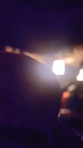 The video shows people in small boats, wearing conical hats and life vests, being rowed through a dimly lit cave. The cave ceiling is visible with light fixtures hanging down. The water is dark and reflects some light.
