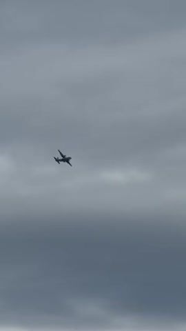 An airplane is flying in the sky. The sky is overcast with clouds. The airplane is in the center of the frame and is silhouetted against the clouds. The airplane appears to be a propeller-driven aircraft. It is flying from left to right across the screen.