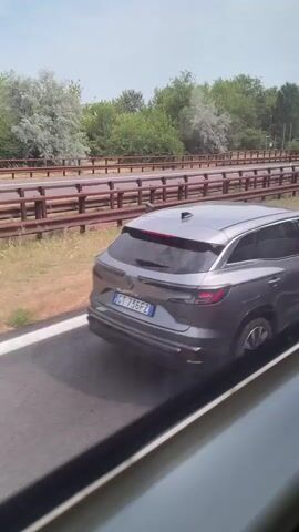The video shows a gray Renault Austral on the highway. The camera is filming from inside a bus or a car, in parallel. Other vehicles can be seen moving on the parallel section of the highway, including a big rig trailer and a light colored Audi A4 Avant. There is vegetation along both sides of the highways.