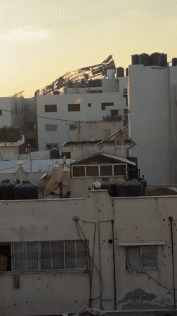 Gaza City skyline at sunset, damage and debris visible across rooftops