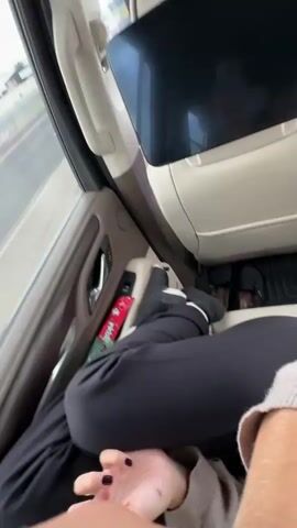 The video, presumably shot from inside a moving vehicle, shows three people. The interior of the vehicle is light beige. The video starts with a shot from the back seat, showing the back of the front passenger seat with a built-in screen.  The camera then pans quickly to the side, revealing a woman in the backseat.  She wears a white top and light beige sweater and makes a kissing face towards the camera. She is wearing a seatbelt. Next, the camera turns to the front passenger seat, where a woman with curly hair sits in a gray sweatshirt. The scenery outside the window suggests they are driving on a highway. The video's orientation is consistently rotated, with the subjects appearing sideways for a portion of the viewing time.