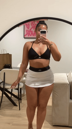 Mirror selfie in a London bedroom, black sports bra and white skirt.