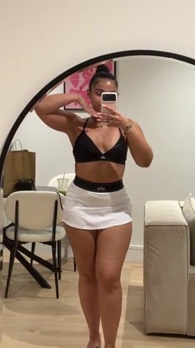 Mirror selfie in a London bedroom, black sports bra and white skirt.