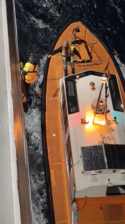 Maritime workers handle illuminated boat in choppy Ibiza waters