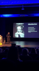Man gives presentation at Pomorie auditorium with blue stage lighting