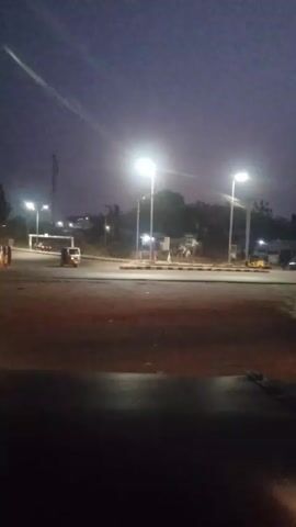 Here's a concise description of the video:

The video shows a street scene at night or twilight.  Several streetlights illuminate a roundabout or intersection.  A three-wheeled vehicle is traveling on the road.  Other vehicles are visible in the distance.  The video appears to be taken from a slightly elevated position.