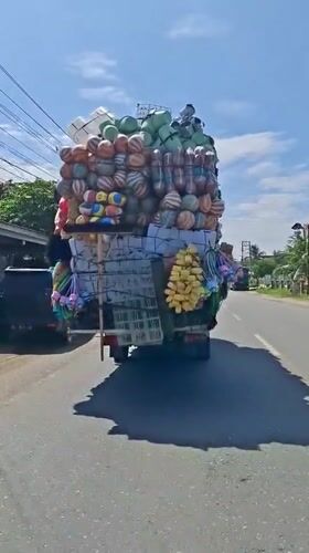 Overloaded truck spotted on Indonesian road near dinosaur statue