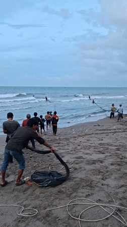 Fishermen pull nets onto beach in Lhokseumawe, Indonesia