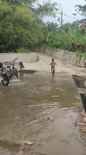 Boy cycles through muddy water crossing in Saweuk