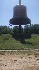 Bronze bell monument with cross and Cyrillic inscriptions on a hill