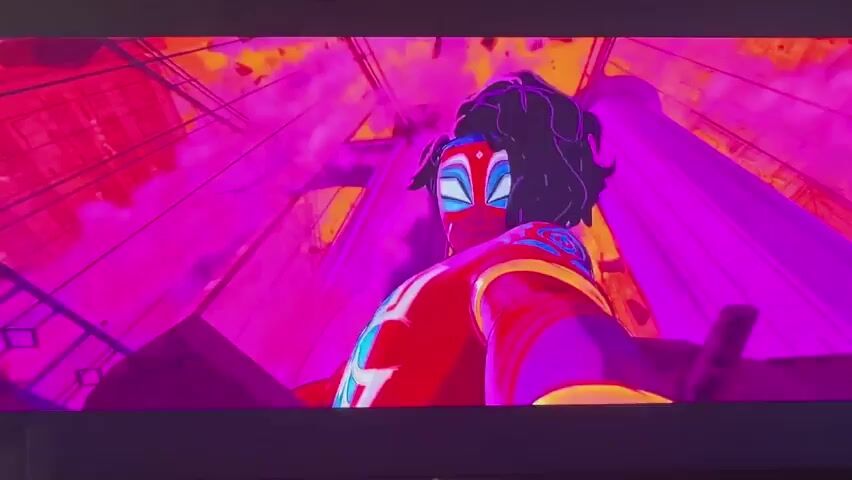 This media file is a short video clip, likely from an animated production, set in a vibrant, stylized urban environment. The dominant colors are bright pinks, purples, and yellows, suggesting a surreal or hyper-real aesthetic.

The clip features several scenes involving animated characters and objects. In the first scene, a character with dark, curly hair and a red and blue costume, resembling a superhero, is shown from a low-angle perspective, looking upwards. They are surrounded by abstract, geometric shapes and pink smoke, with tall, angular structures in the background.

The second scene shifts to a different perspective, showing a character in a red and yellow outfit lying on the ground, with what appears to be a hand reaching out from the foreground. The background remains colorful and somewhat indistinct, with hints of elevated structures.

The third scene shows the same character lying on the ground, appearing to be unconscious or injured. The surrounding environment shows people silhouetted in the background, and more of the colorful, angular architecture.

The final scenes depict a street scene with two large trucks, one purple and one yellow. A person is kneeling between them, interacting with something on the ground. The setting appears to be a city street, possibly at night or during a period of unusual lighting, given the intense colors. There are no visible text elements within the clip. The overall mood is energetic and action-oriented, typical of a superhero or action-adventure genre. The stylized animation and vivid color palette are the most prominent features.