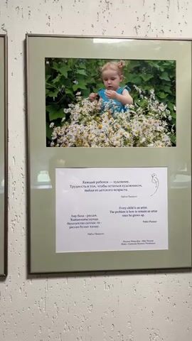 The video shows a person walking along a wall with framed photos hanging on it. The photos depict children, and each is paired with a quote related to childhood or art. The quotes are written in Russian, English, and another language. The walls appear to be painted with a speckled pattern.