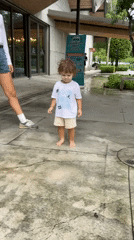 Toddler walks on wet pavement near overcast beach