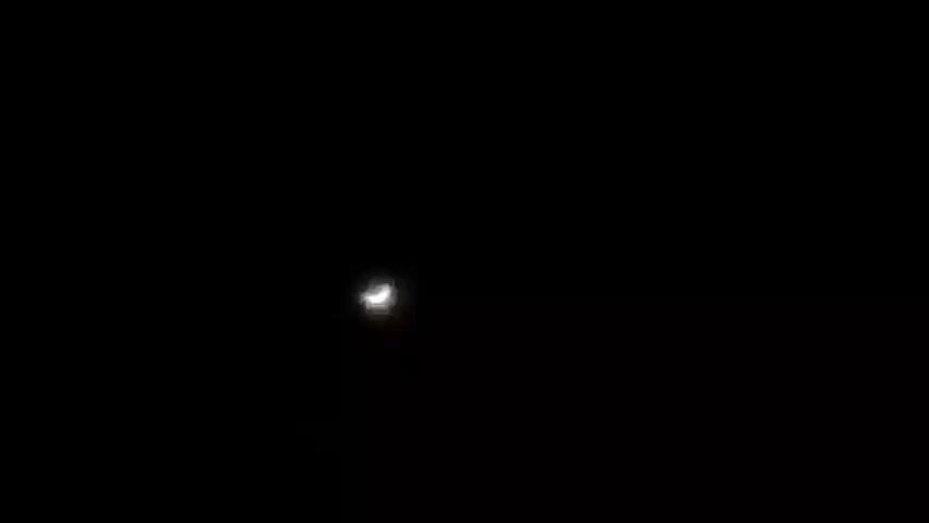 The video shows a sliver of the moon in a black sky. The moon is illuminated from the right, with the left side of the moon appearing dark. The moon is small and slightly out of focus in the center of the frame. The video is dark, with the moon being the only visible object.