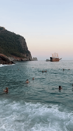 Swimmers, waves, and a tall ship off the Alanya coast