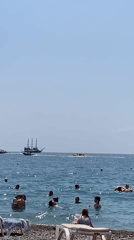 Summer morning on Kemer's beach: swimmers, parasailing, and boats offshore.