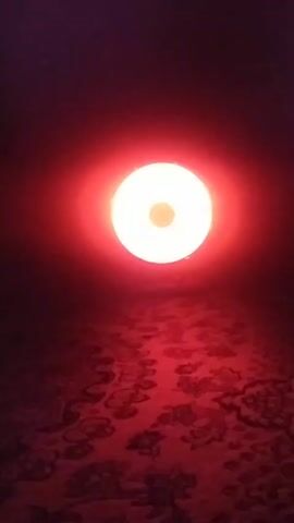 A dimly lit room is illuminated by a round, white light source.  The light is centrally positioned, radiating a soft glow that casts a red hue across the room.  A red carpet with a repeating floral pattern covers the floor, with the light reflecting off of it.  The room otherwise appears dark and featureless.  A human voice is audible in the background.