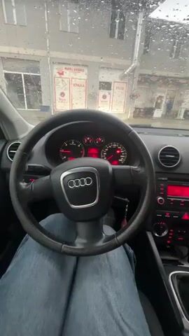 The video shows the interior of a car. The first shot shows the driver's perspective, with the steering wheel and dashboard visible. The second shot is a close-up of the dashboard and radio. The third shot shows a woman in the passenger seat taking a selfie, making a peace sign and sticking out her tongue. The final shot shows the woman's hand reaching out towards the dashboard, with a charm hanging from the rearview mirror. The weather outside appears to be rainy.