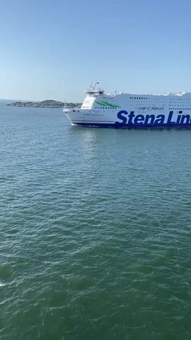 A large Stena Line ferry sails across calm green water under a clear blue sky. The ferry is white with a blue Stena Line logo and green accents. The water is slightly choppy. The bow of the ferry is visible on the left side of the frame, and the stern is on the right. The ferry appears to be in motion.