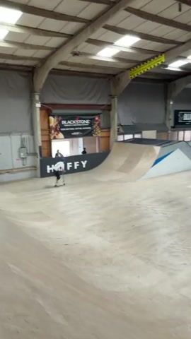 Here is a description of the video:
The video shows a person riding a scooter in an indoor skatepark. The person is wearing a helmet, a white shirt, and dark shorts. They ride up a ramp and perform a trick, jumping high into the air before landing back on the ramp. The skatepark has various ramps and obstacles. The video also shows the logos of HUFFY, BLACKSTONE, and BLUNT Scooters displayed on the walls. A caution sign is visible hanging from the ceiling.