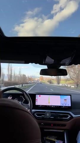 The video shows a first-person perspective of driving a car on a highway. The car has a sunroof, and the sky is visible. The driver is using a navigation system on the dashboard, and music is playing. Other cars and trucks can be seen on the road. The landscape includes trees and fields. The speedometer indicates varying speeds around 160 km/h.
