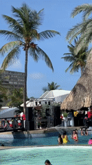 Crowded resort pool party with DJ and stage in Porlamar