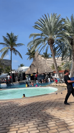 Crowded resort pool party with DJ and stage in Porlamar
