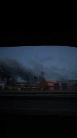 The video shows a view from inside a vehicle, looking out through a side window. The scene outside is a highway landscape at dusk or dawn, with a dark blue sky filled with heavy, ominous-looking clouds. There are buildings, billboards, and streetlights visible alongside the highway. The camera appears to be moving as the vehicle drives along the road.