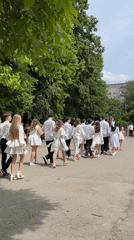 Graduates in white formal wear process through Ternopil courtyard
