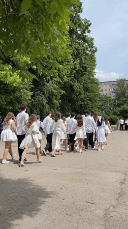 Graduates in white formal wear process through Ternopil courtyard