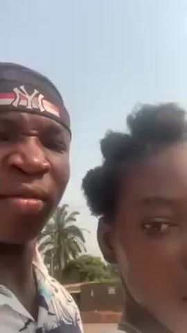 Here is a description of the video.

The video shows three young people walking outdoors on a bright day. The camera is held by one of the individuals, a young man wearing a patterned shirt and a black head wrap with white lettering and red and white decorative elements. He turns the camera occasionally to show the other two people walking with him. One appears to be a young woman with her hair styled in small buns. She wears a white shirt. The third person, a young man, is wearing a brown shirt with yellow stripes at the shoulders. In the background, there are utility poles with lines, as well as trees.