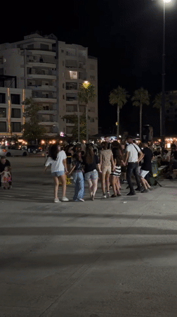 Circle dancing at night in Vlorë's lit outdoor streets