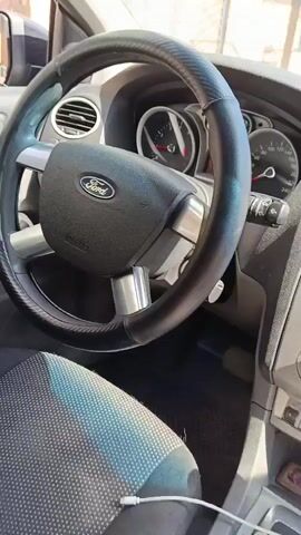 The video shows the interior of a car. The camera pans across the steering wheel, dashboard, gear shift, and the passenger seat. A bottle of orange liquid is visible on the passenger seat. The car appears to be parked, as indicated by the gear shift being in the 'P' position. The lighting suggests it is daytime.