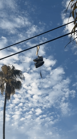 Worn sneakers dangling from a wire under a LA sky.