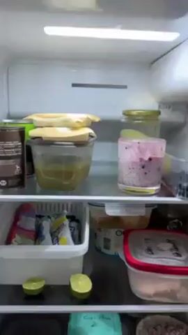 The camera pans down inside a refrigerator showing four shelves and two shelves on the door. The refrigerator appears to be full. The top shelf contains glass and plastic containers with unknown contents, as well as several halves of limes. The second shelf contains more plastic containers with unknown contents. The third shelf contains various plates with covered food items. The fourth shelf contains jars and bottles. The first door shelf contains jars and bottles as well as a champagne bottle. The second door shelf contains cartons of what appears to be yogurt.