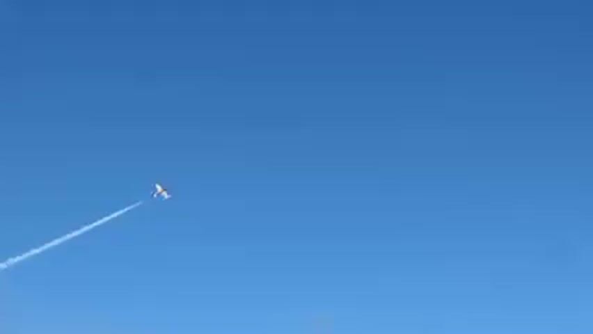 A small plane flies diagonally across a clear blue sky, leaving a white contrail behind it.