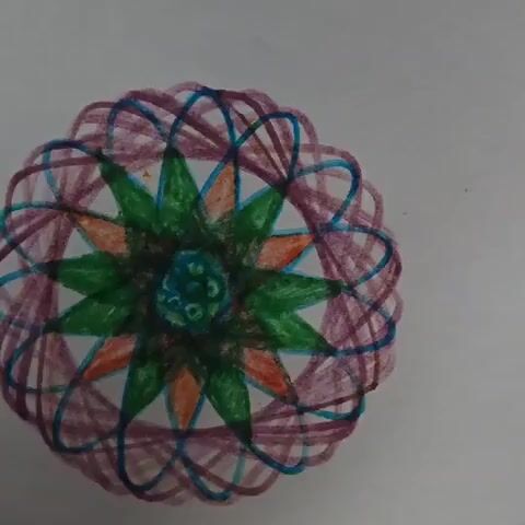 The video shows an abstract circular drawing in various colors on a white surface. The inner design consists of green, orange, and blue shapes, radiating outwards. The outer part is made of curved lines in purple and blue, resembling a sphere. No people are visible.