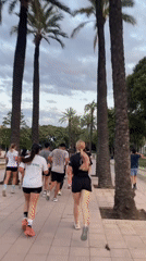Group jogs palm-lined path in Valencia under pink-hued skies