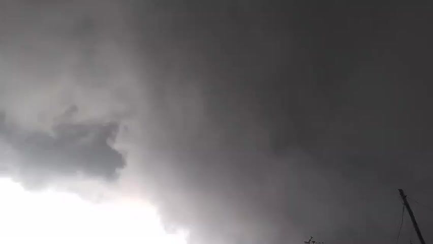 The video shows a very dark and stormy sky. The clouds are heavy and gray, and the light is dim. There is a utility pole and antenna silhouetted against the sky.