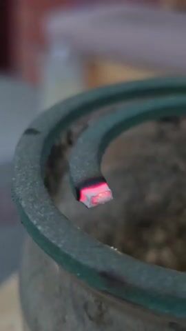 The close-up footage shows a burning mosquito coil in a spiral pattern. The coil is gray and rests within a larger, dark gray, circular object that appears to be an ashtray or holder. The end of the coil is glowing red and emitting a faint wisp of smoke, indicating it is actively burning. The background is softly blurred, with hints of muted colors that suggest an indoor setting. No people are clearly visible, though a hand holding the camera is partially in the frame at the top. The overall tone is neutral, focusing on the detail of the burning mosquito coil. There is no visible text in the media file. The time of day and weather conditions are not discernible. The context provided states the location as Nova Kakhovka, Ukraine.