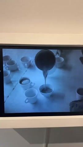 The video displays a series of close-ups of cups on a table. Initially, liquid is poured from a pitcher into a cup. This is followed by scenes of children drinking from cups. One young girl with a bow in her hair is shown holding and drinking from a cup while also holding a large slice of something, possibly cake or pie. Then, three boys are seen drinking from cups. The first boy is looking to his left, while the other two are focused on their drinks. The scene appears to be indoors, possibly a dining hall or a room with tables. The overall tone suggests a communal meal or a break, with the children engaged in drinking. The video is black and white, which could indicate it is archival footage. There is no visible text within the video frames. The provided location context of Bern, Switzerland, doesn't offer any specific visual cues within the video itself, as the setting appears generic. The time of day and weather are not discernible from the images. The emotions of the children seem neutral or content as they are drinking.